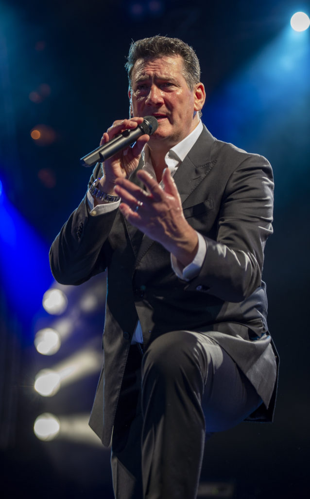 Tony Hadley canta con microfono, vestito con camicia bianca e abito grigio