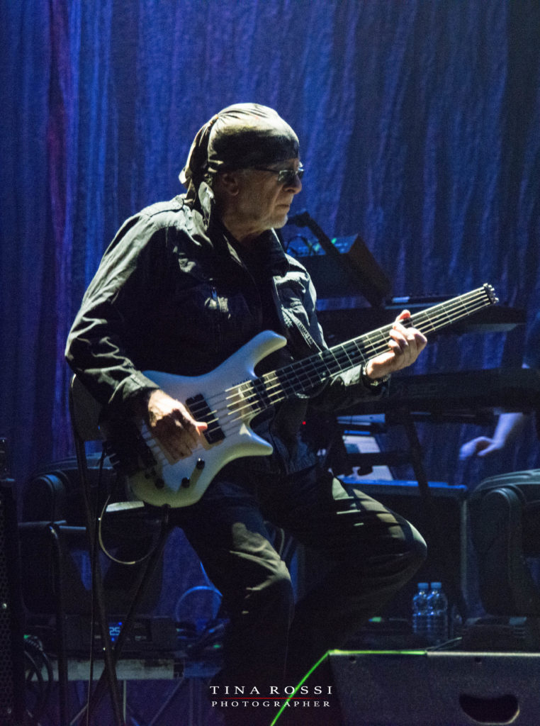 primo piano di Patrick zivas, bandana nera sul capo, bassista della pfm, basso bianco a cinque corde