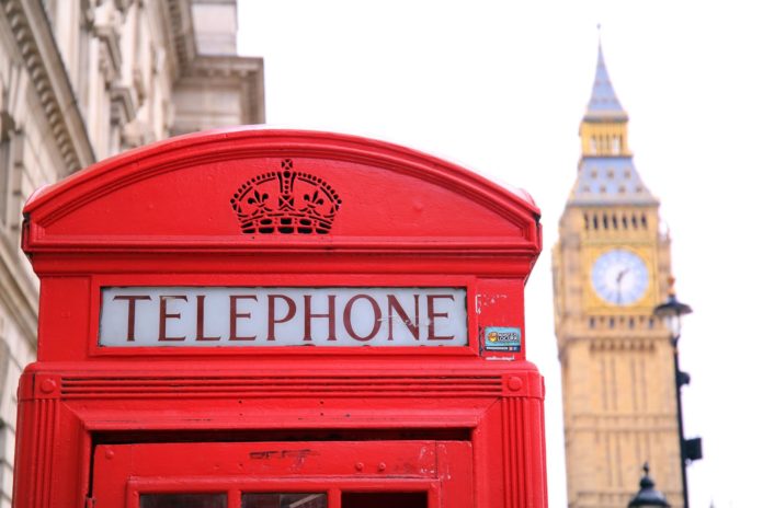 Primo piano di una tipica cabina telefonica inglese, sullo sfondo la torre di Londra