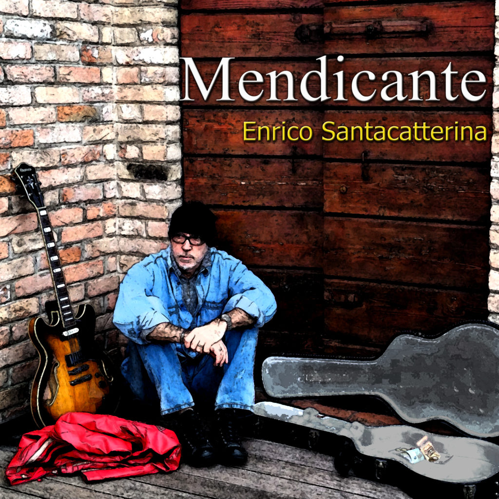 copertina album blues "il Mendicante": nella foto Enrico è seduto in un angolo tra un muro e un portone di legno di fianco a lui una chitarra appoggiata al muro e dall'altra parte la custodia dello strumento aperta.Ai suoi piedi una felpa rossa