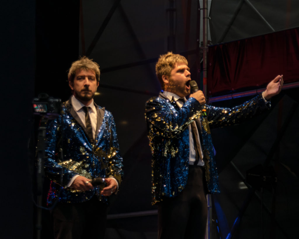 Paolo Ruffini e David insieme sul palco vestiti uguali, con la stessa camicia bianca, cravatta nera e giacca di lamè azzurra e dorata