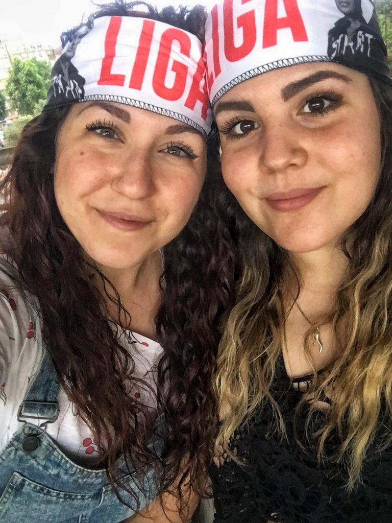 Due giovani ragazze con i capelli lunghi sorridenti, con la fascetta sulla fronte con scritto ligabue