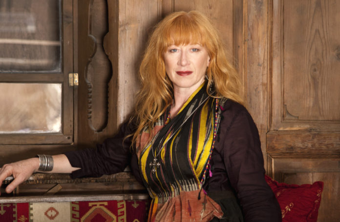 loreena mckennitt in primo piaano con i capelli lunghi e rossi seduta davanti a un tavolo