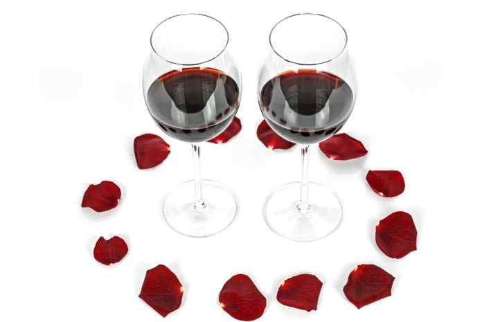 due calici di vino rosso circondati da petali rossi di rosa