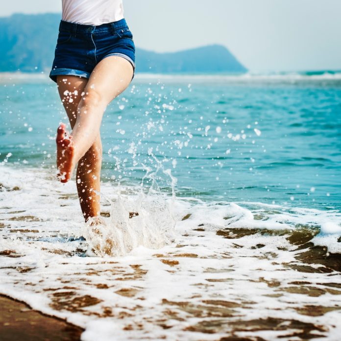 attività estive nella foto delle gambbe di donna che tirano un calcio all'acqua di un'onda del mare
