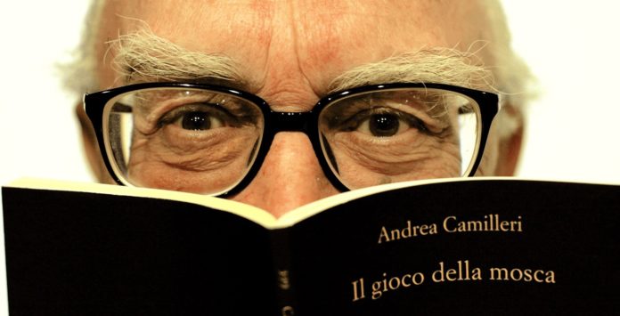 Primo piano di Andrea Camilleri, autore del commissario Montalbano. Limmagine rappresenta il volto con gli occhiali ed un libro che gli copre il viso fino al naso. Sulla copertina del libro la scritta Andrea Camilleri 