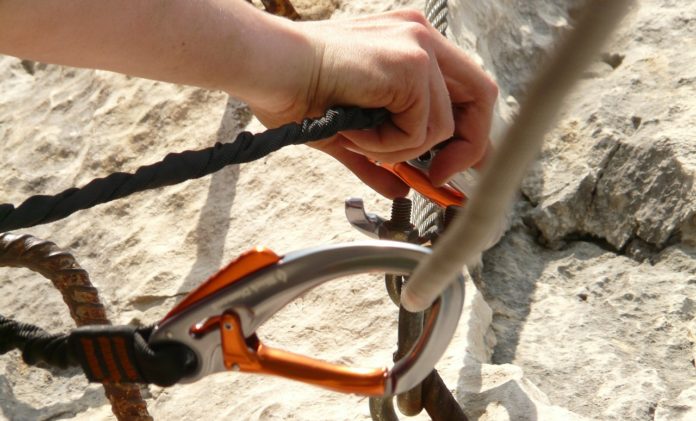 mano intenta ad agganciare una serie di corde a dei ganci utilizzati per il free climbing