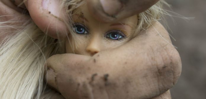 A simbolo della violenza sulle donne,una mano sporca di terra stringe la testa di una barbie con gli occhi azzurri