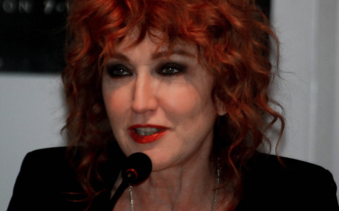 Fiorella Mannoia con i capelli rossi e una giacca nera parla davanti a un microfono in conferenza stampa