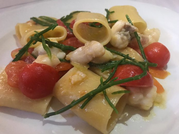 piatto di pasta di paccheri conditi con pomodoro pesce e erbette