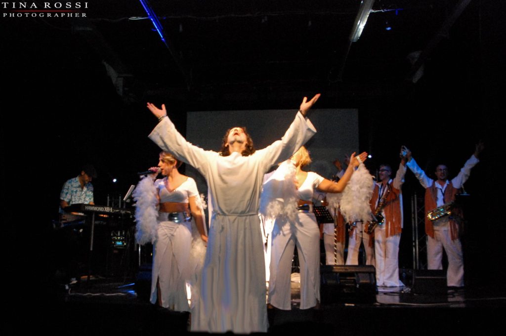 primo piano della coreografia relativa a jesus christ superstar con l'interprete di Gesù a braccia alzate