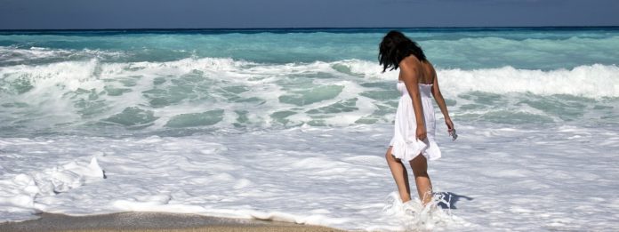 felicità di un pensiero lontano, nella foto una ragazza vestita di bianco cammina sulla riva del mare con le onde che si infrangono