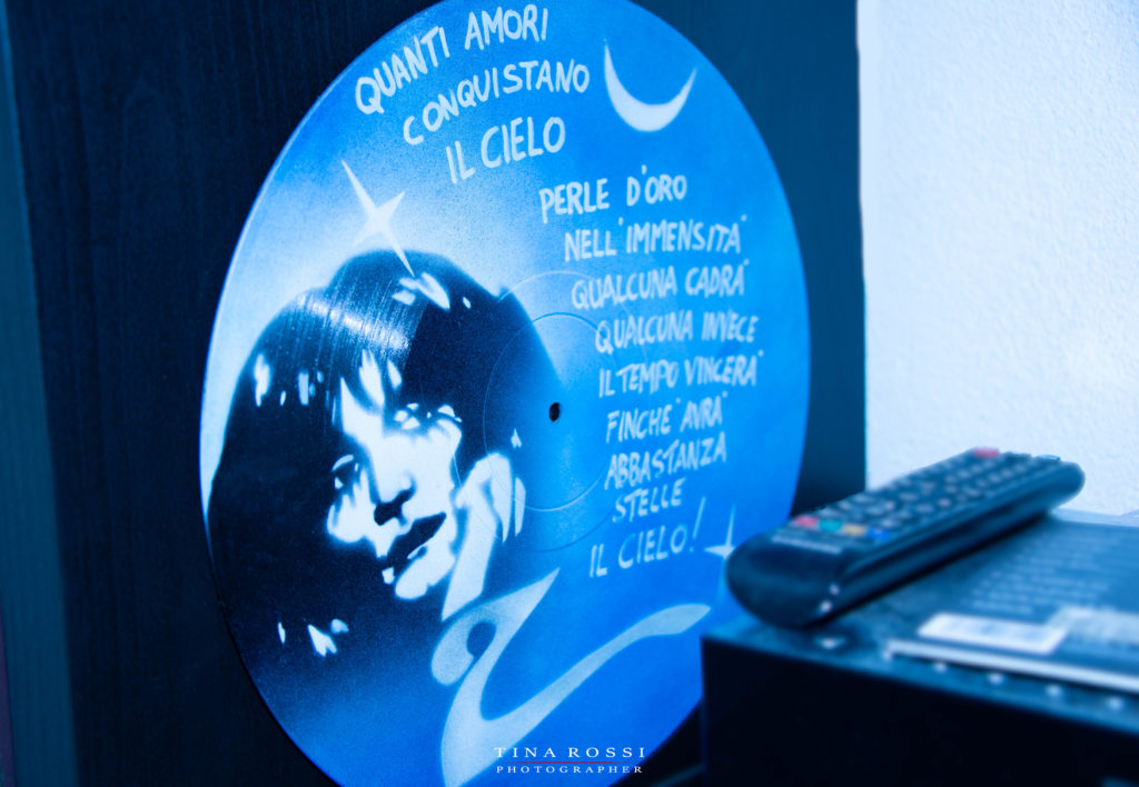 Nella foto un vinile azzurro disegnato a mano riporta il viso di Renato Zero e una scritta tratta dal brano "il cielo"