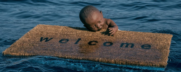 Immigrazione: quando l’arte diventa provocar(t)e. primo piano di un bimbo di colore aggrappato ad uno zervino con la scritta welcome