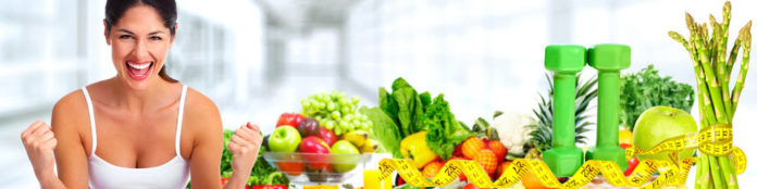 allenamento e alimentazione espressi nella foto con una ragazza in canottiera bianca che alza i pugni sorridendo e vicino a lei un tavolo pieno di frutta e verdura