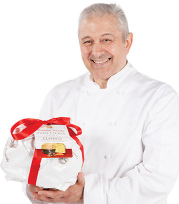 Immagine di Ferdinando Tammetta vestito con divisa bianca da pasticciere tiene in mano il suo panettone artigianale confezionato con carta bianca e fiocco rosso