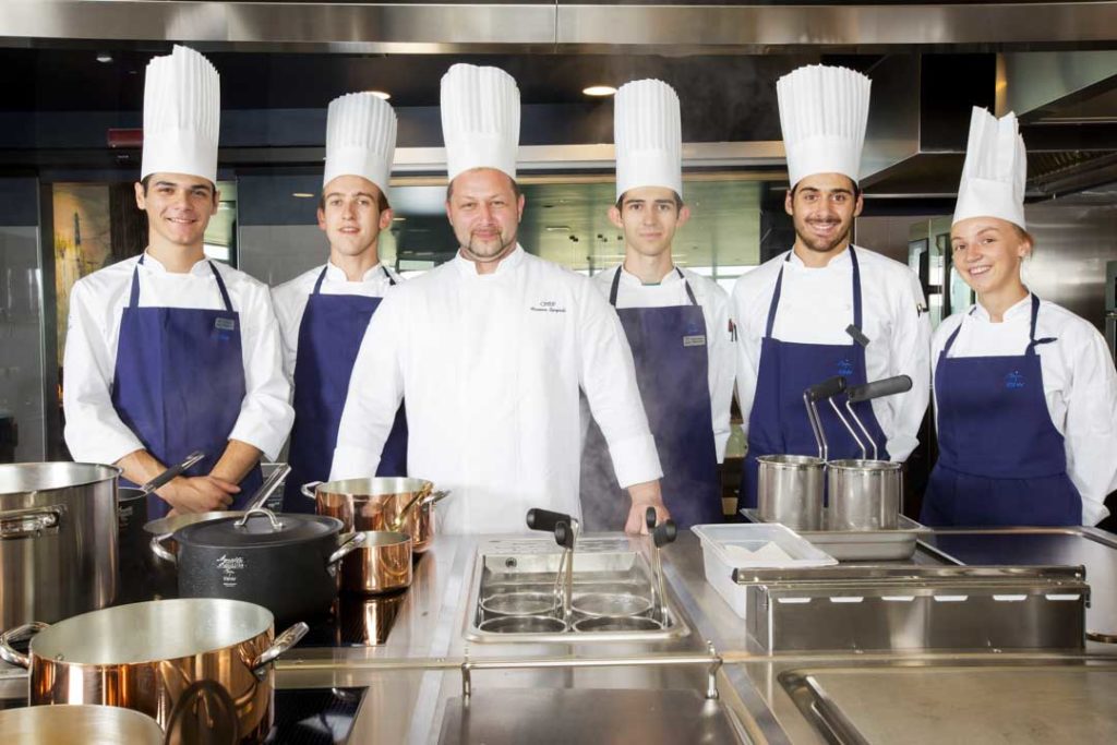 lo staff della cucina del mi view composto da 5 cuochi con cappello bianco e grembiuli scuri davanti al ripiano delle cucine