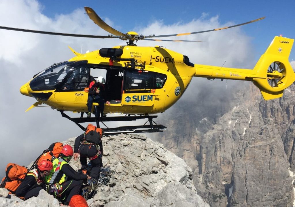 nell'immagine, un elicottero del soccorso alpino con una squadra durante un salvataggio su alcune vette rocciose