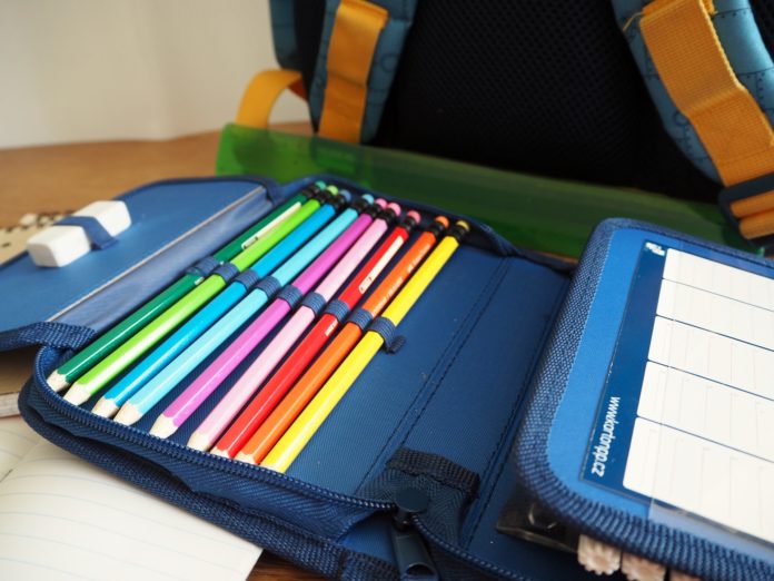 calendario scolastico con un portaspenne aperto pieno di matite colorate e dietro uno zaino di scuola