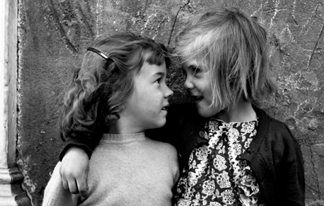 Foto in bianco e nero di Vivian Maier : due bambine, una bionda, una mora , si guardano di profilo, abbracciandosi