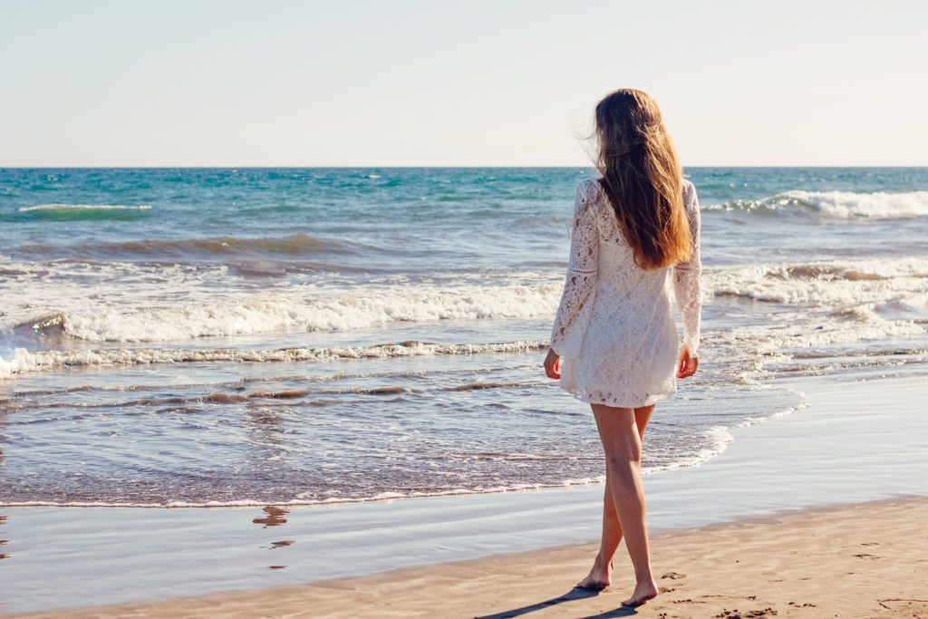 Ragazza in piedi di schiena, vestita di  bianco, che guarda il mare