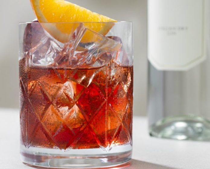 affinity cafè propone in foto un bicchiere dinegroni dal colore tipico rosso e sullo sfondo una bottiglia di gin