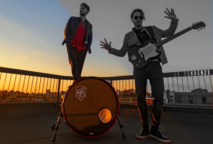 Le Tendenze: in primo piano il duo musicale milanese, su un terrazzo al tramonto, preceduti dalla grancassa di una batteria