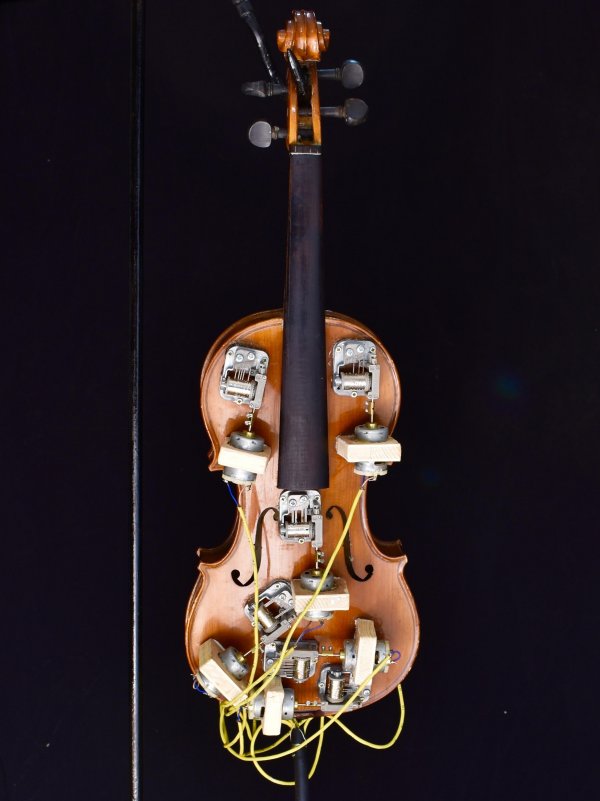Arte al maker faire con Un violino  in legno arricchito con contatti meccanici multimediali. Cilindri e fili gialli lo ricoprono interamente. 