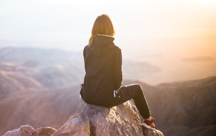 donna seduta su un masso su una montagna ad un passo da un burrone, guarda il tramonto