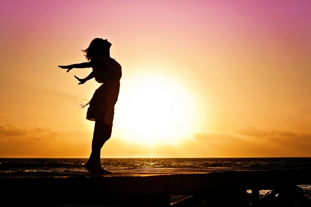 Una donna di profilo, sul bordo del mare con le braccia protese all'indietro, in un bellissimo tramonto esprime le sue emozioni di libertà e felicità