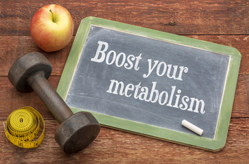 Il metabolismo è la base della nostra forma fisica "boost your metabolism" scritto su una lavagetta con vicino un peso da palestra, una mela e un metro da sarta