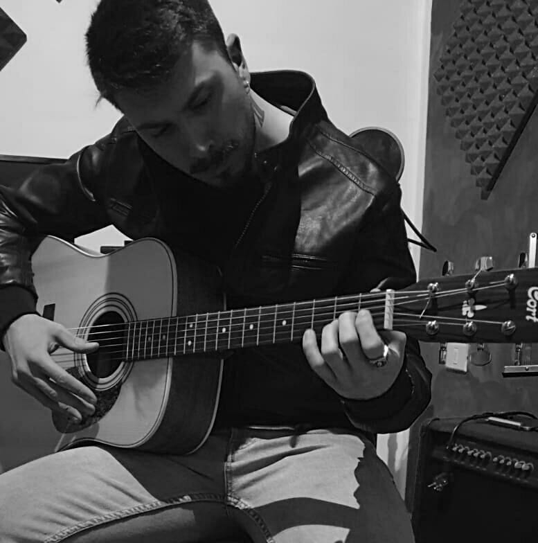 Francesco Setta mentre suona la chitarra classica seduto, con giubbottonero. Foto in bianco e nero 