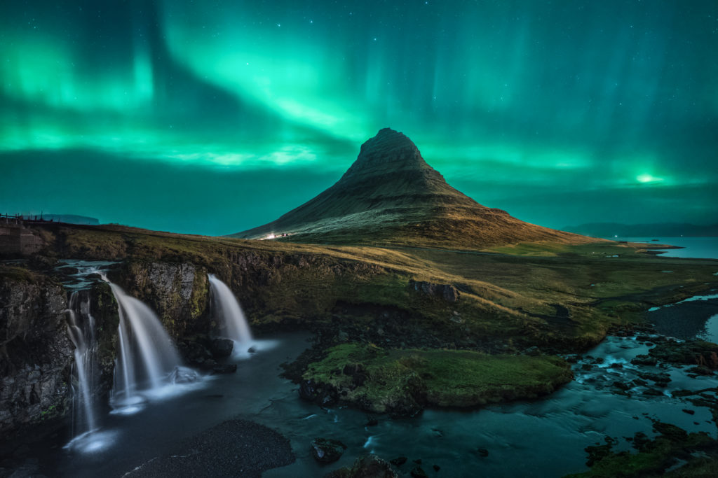 l'aurora boreale in °Islanda con un cielo che si colora di verde e il paesaggio sembra lunare, con cascate di acqua e torrenti azzurro viola