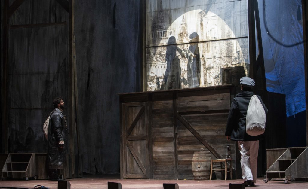 Un frame della scenografia di Sweeney Todd che rappresenta il portodiLondra condelle casse di legno, una botte, due scalette ai lati e due personaggi con il sacco sulle spalle
