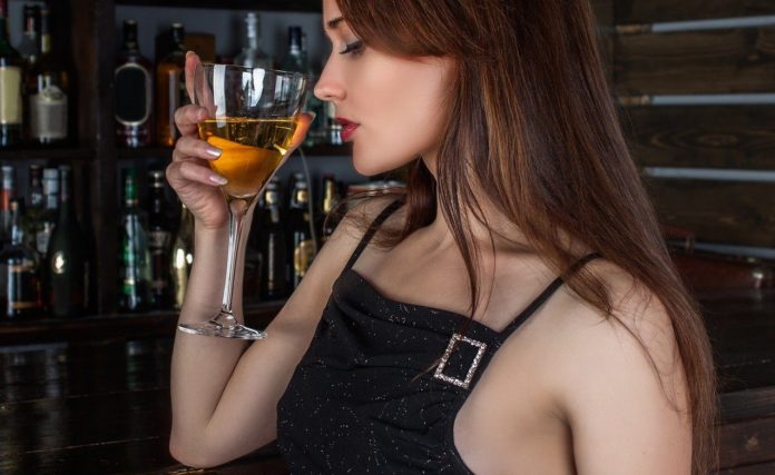 Donne e vino, nella foto una ragazza con abito da sera beve un bicchiere di vino