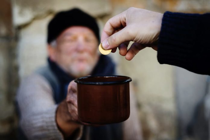 una mano mette due euro nella tazza di un povero