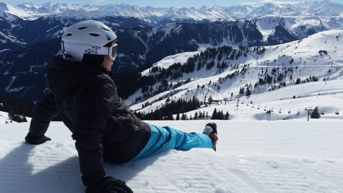 un bambino seduto sulla neve guarda la montagna e gli sciatori durante la vacanza di natale