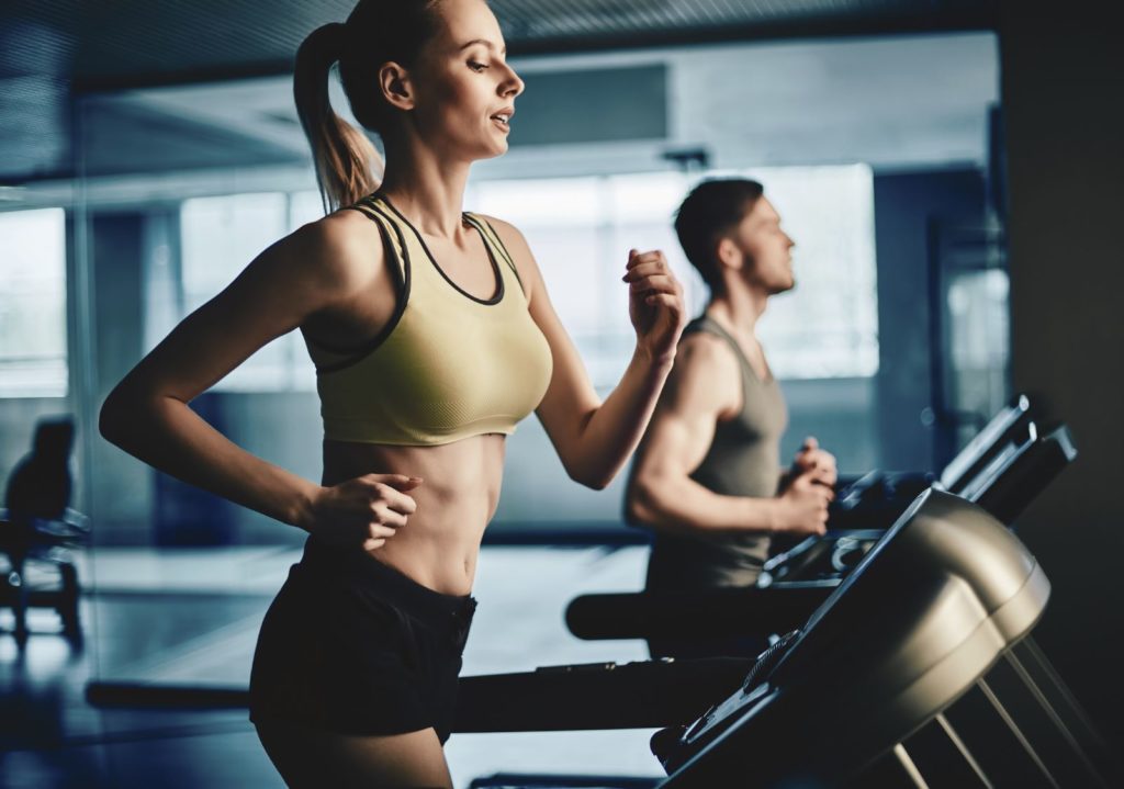 una donna in top giallo che corre sul tapis roulant per fare esercizi cardio per il corpo