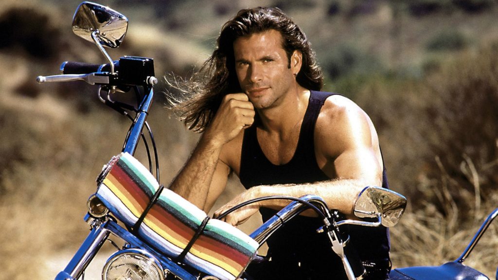 Harleysta: primo piano di Lorenzo Lamas, appoggiato al manubrio della sua Harley-davidson. indossa una canotta nera