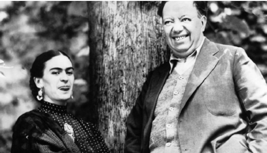 foto in bianco e nero di Frida Kahlo e Diego, l'uomo della sua vita, in piedi vicino ad un albero che sorridono verso l'obiettivo divertiti