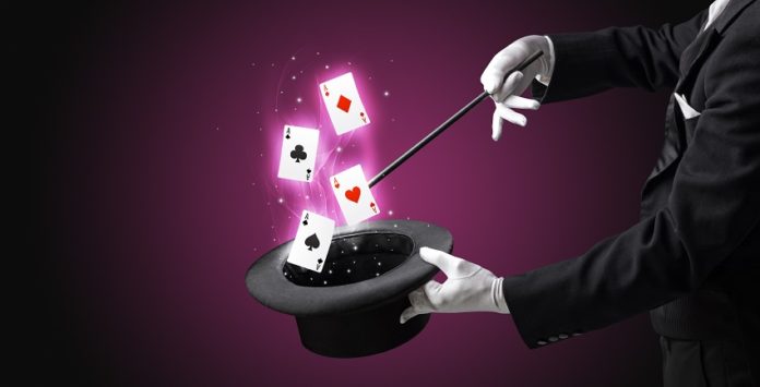 un mago con guanti bianchi fa la magia di tenere sospese delle carte da gioco su un cilindro durante uno spettacolo