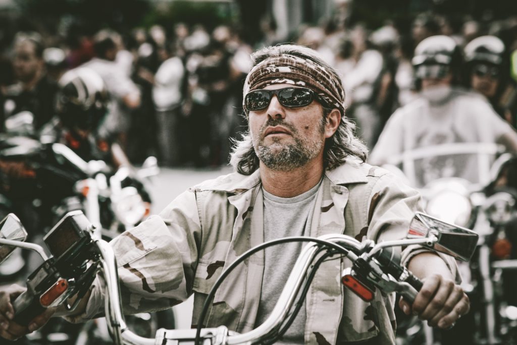 Harleysta: in primo piano un motociclista, con giubbotto di jenas grigio e occhiali da sole
