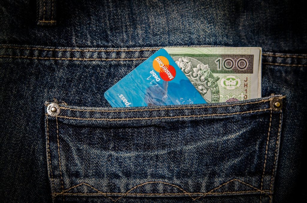 una tasca di un jeans dalla quale spuntano una carta di credito e dei soldi sindrome da shopping