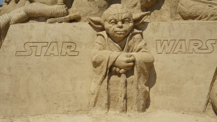 Yoda il personaggio di Star Wars fatto con la sabbia, è piccolo, con lunghe orecchie da elfo e ha le mani appoggiate su un bastone