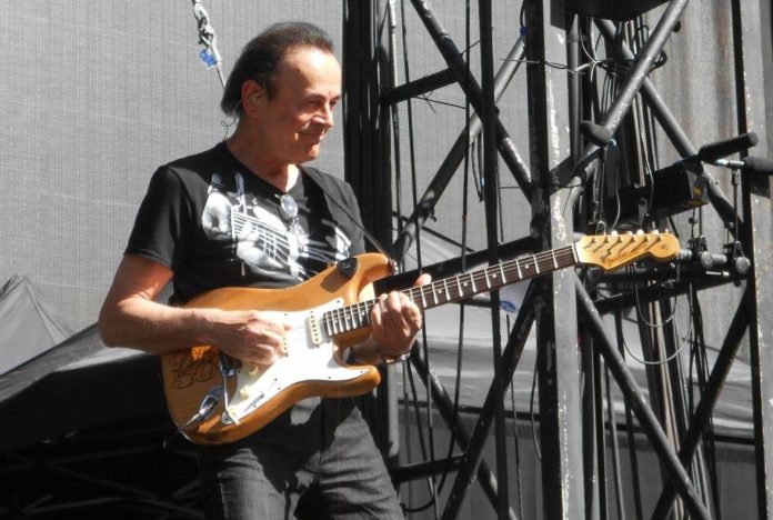 Dodi Battaglia sorrdendo suona la chitarra con jeans scuri e t shirt