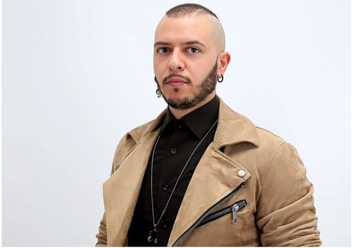 Marco Sentieri con camicia nera e giacca beige con la scritta Sanremo giovani