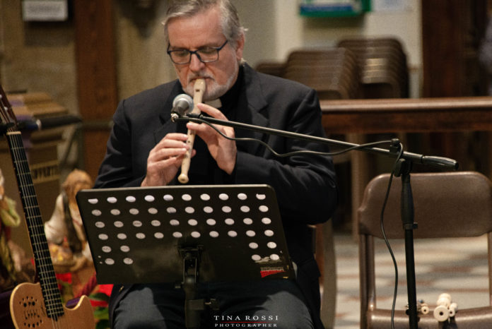 Don Carlo fonde insieme Chiesa e musica suonando un flauto seduto davanti a un leggio, come discusso nel convegno pontificio di novembre