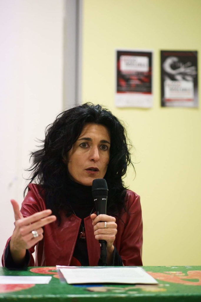La psicologa Henni Rissone spiega la pulsione alla violenza. Giubbotto rosso seduta al tavolo durante un convegno
