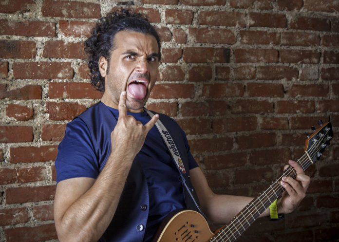 BAZ Marco Bazzoni nello show la verità rende single con t shirt blu, fascia sui capelli chitarra alla mano, bocca aperta e lingua di fuori e con la mano destra ma le corna