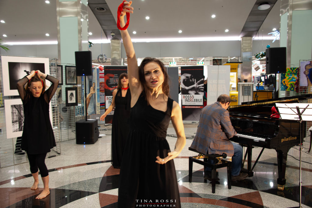 Rosalba Castelli nella performance per muta la pelle, sulla violenza sulle donne, vestita di nero tiene nela mano alzata un fazzoletto rosso